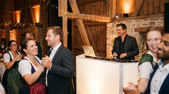 DJ-Pult in einer Scheune, dahinter tanzen Hochzeitsgäste (Symbolbild)