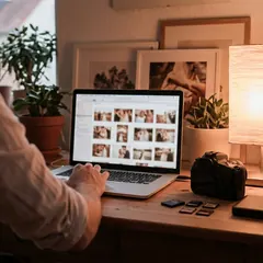 Fotograf bearbeitet Hochzeitsfotos am Schreibtisch, auf dem Laptop eine Galerie mit Vorschaubildern (Symbolbild)