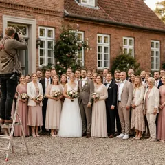 Fotograf auf einer Trittleiter fotografiert die Hochzeitsgesellschaft vor einem Backstein-Gutshaus (Symbolbild)