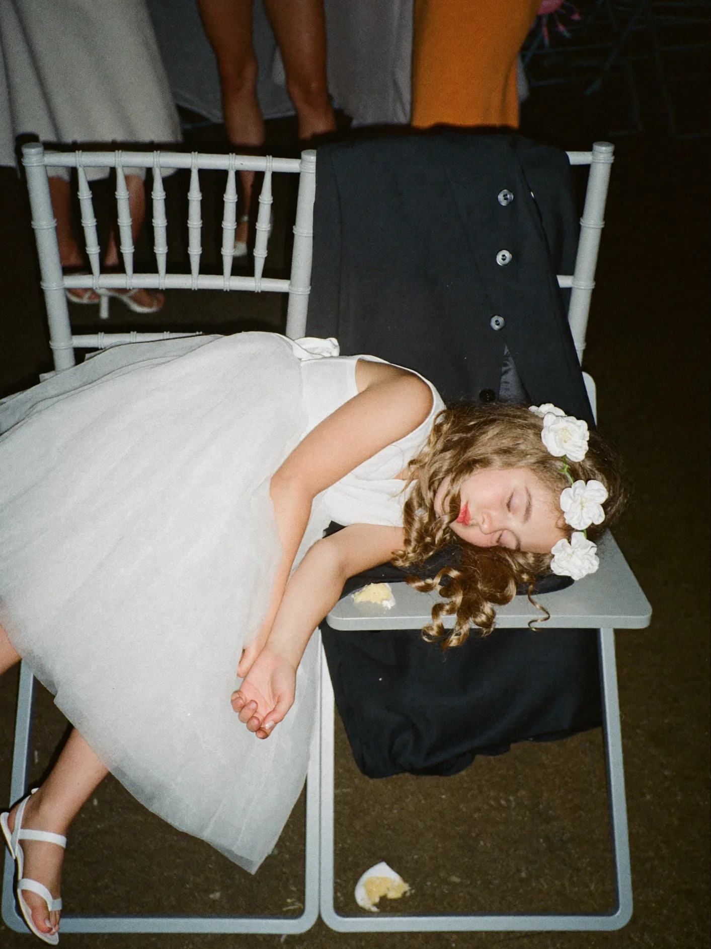 A flower girl asleep on chairs late in the wedding reception